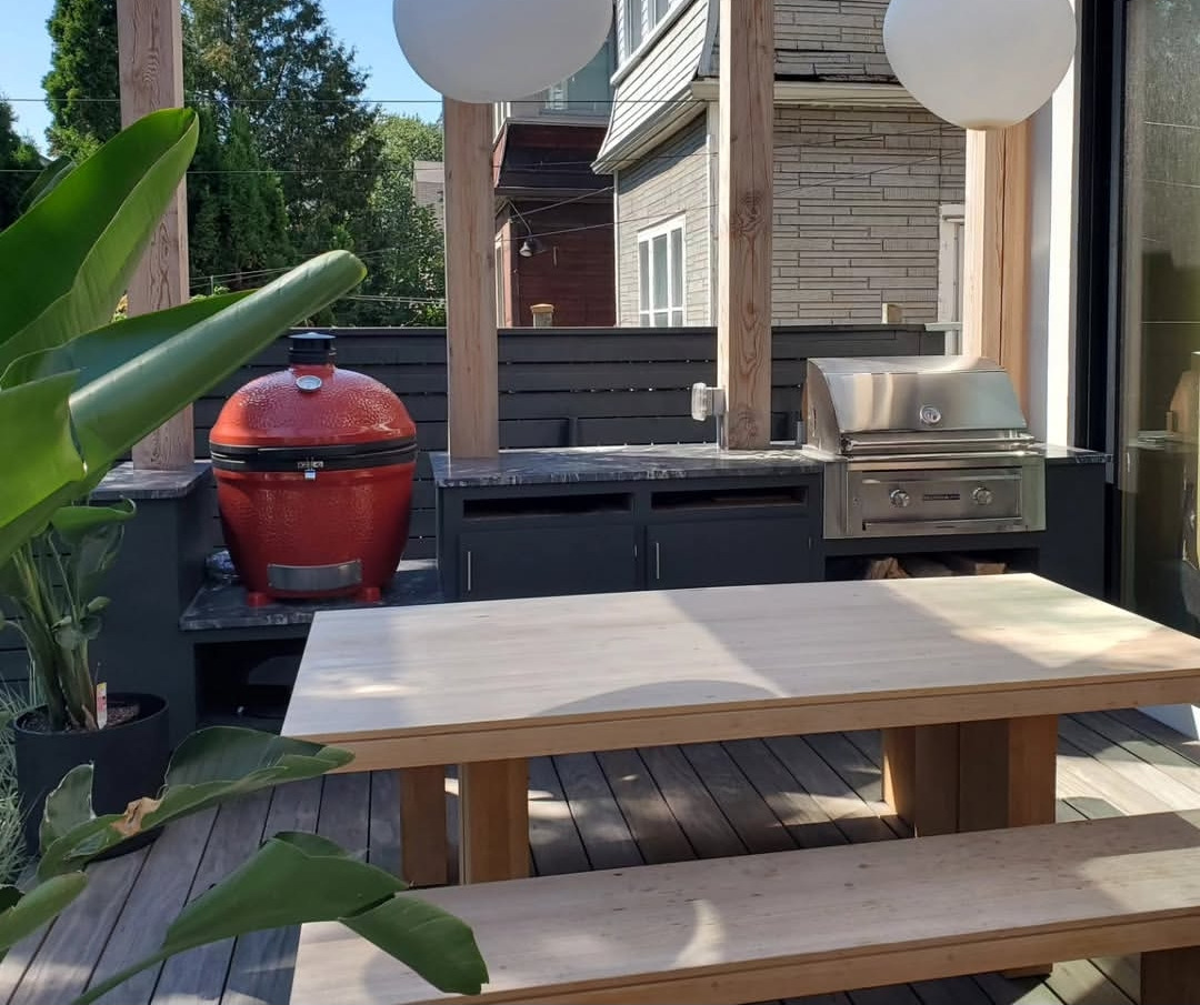 The finished outdoor kitchen in use, with kamado, gas grill, dining table and overhead globe lighting