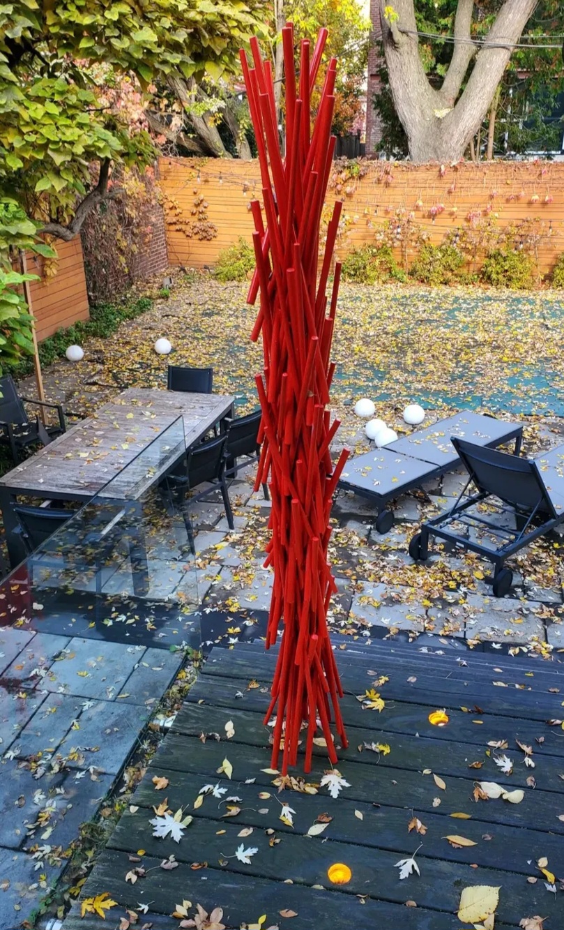 The red rod sculpture in daylight, on the deck among fallen autumn leaves